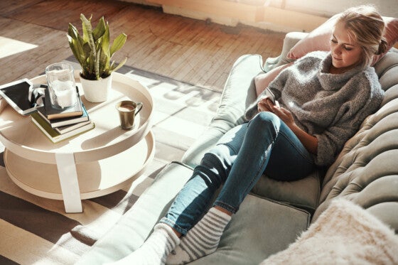 Shot of a young woman relaxing on the sofa at home and using her phone