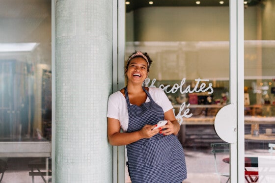 Cafe owner smiles in front of her restaurant, phone in hand