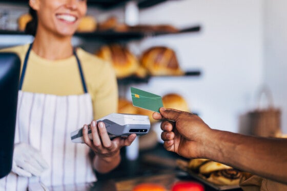 Close-up of a customer using a credit card for contactless payment in a friendly bakery. Smiling cashier holding card reader during transaction.