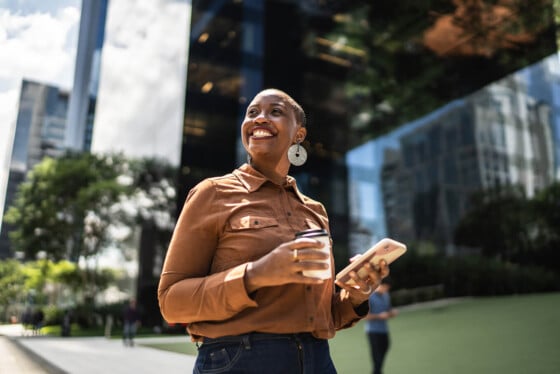 Woman walking with confidence through downtown walkway with coffee and phone