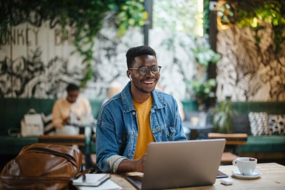 African American man working on laptop in chic coffeehouse, with buds and tea cup