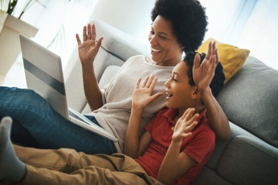 Closeup side view of an african american woman with her son using laptop and staying in touch with their family during corona virus quarantine. They are waving at the screen