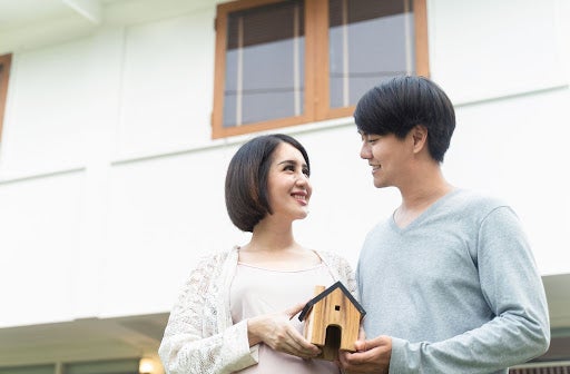 Asian new married couple hold small house toy standing in front of home. Husband and young pregnant wife buy real estate for stay with future newborn baby in family together. Mortgage property concept