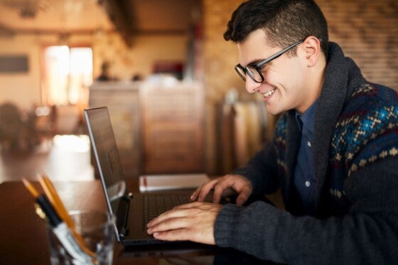 Smiling freelancer businessman working on laptop in cafe. Blogger updating his profile in social networks with photos sharing with followers multimedia using notebook with wifi.