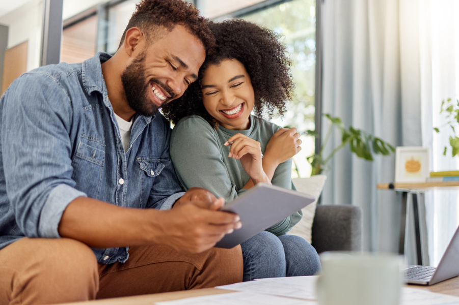 Black couple sitting in living room looking at tablet device.