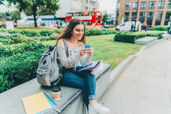 college student sitting on a bench looking at her rewards checking account