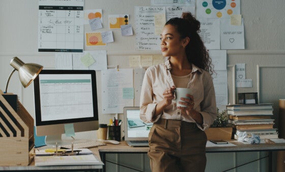 Young businesswoman standing and looking contemplative while holding a cup of coffee in her home office