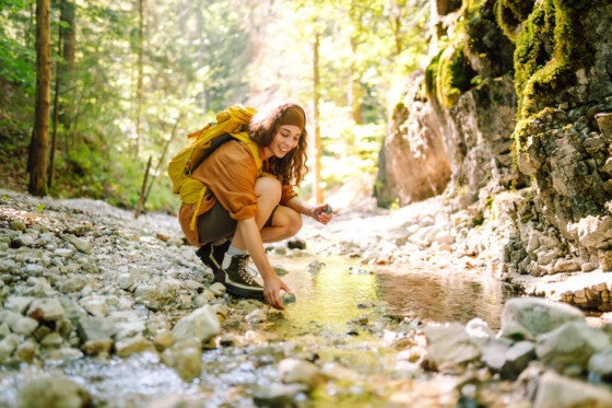 Woman draws clean spring water from the mountain creek. Travel, adventure. Concept of an active lifestyle.
