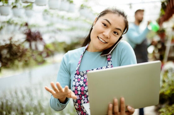 Young Attractive Asian Woman Working at the Plants Nursery Using Smartphone and Laptop