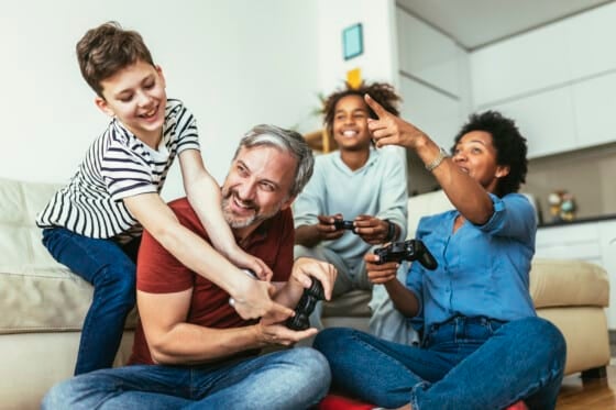 Smiling family enjoying time together at home sitting on sofa in living room and playing video games.