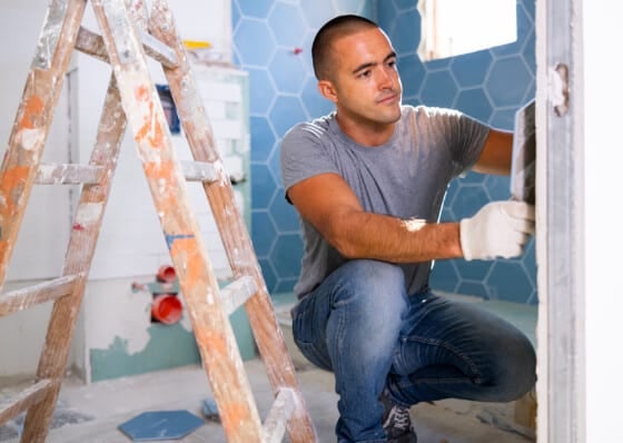 The technology of laying tile, repair and decoration. Focused man wearing ordinary clothes puts porcelain tiles on wall sitting squat at bathroom