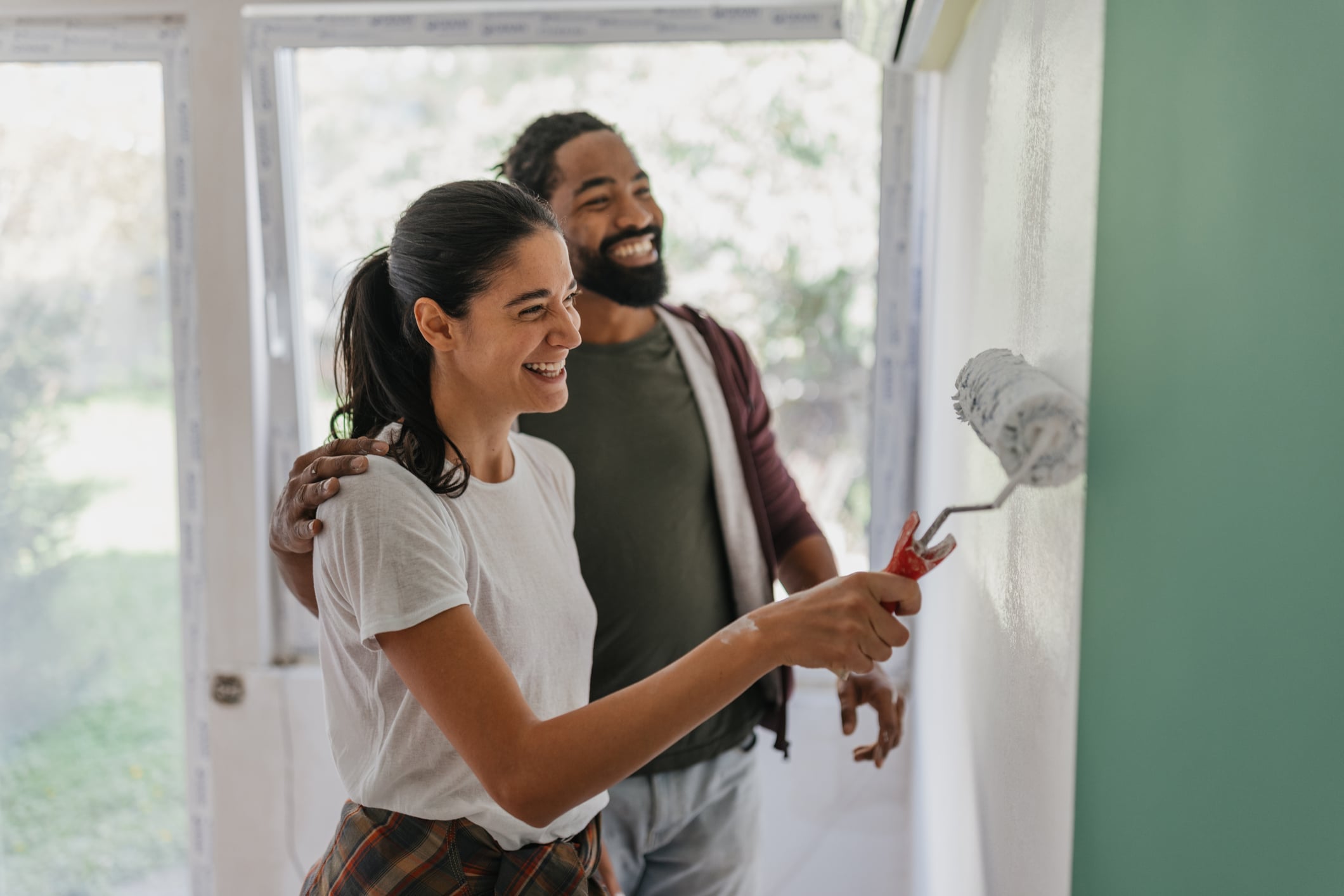A couple paints a wall together, bringing color and positivity to their home while sharing a lighthearted moment filled with joy, creativity, and partnership.