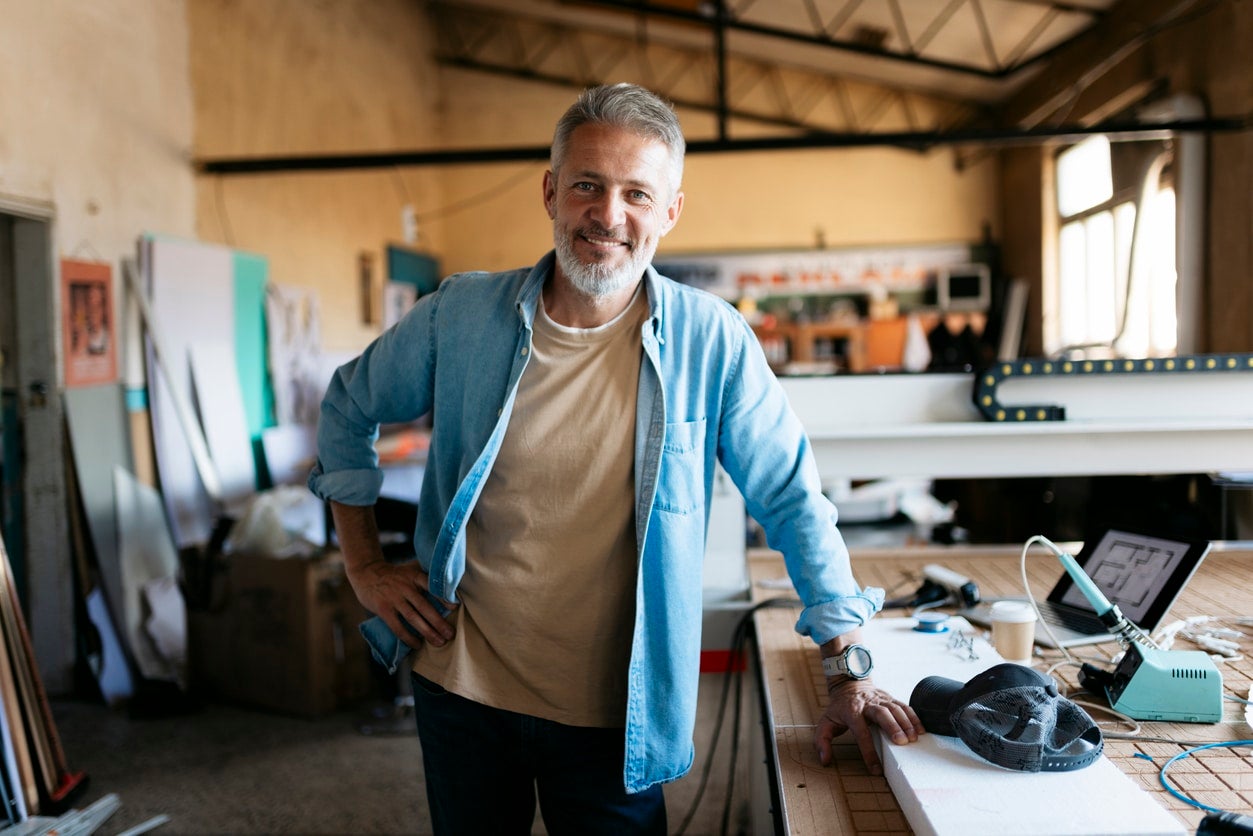 Portrait of a mature engineer smiling in his workshop, posing next to his 3d printer